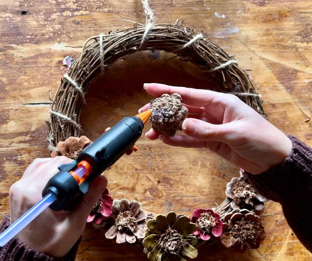 image shows using glue gun to attach pinecones to wreath.