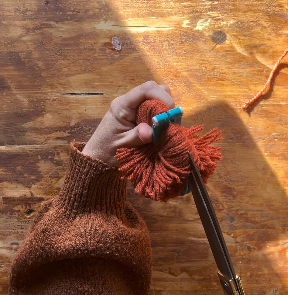 image shows cutting pom pom with scissors.