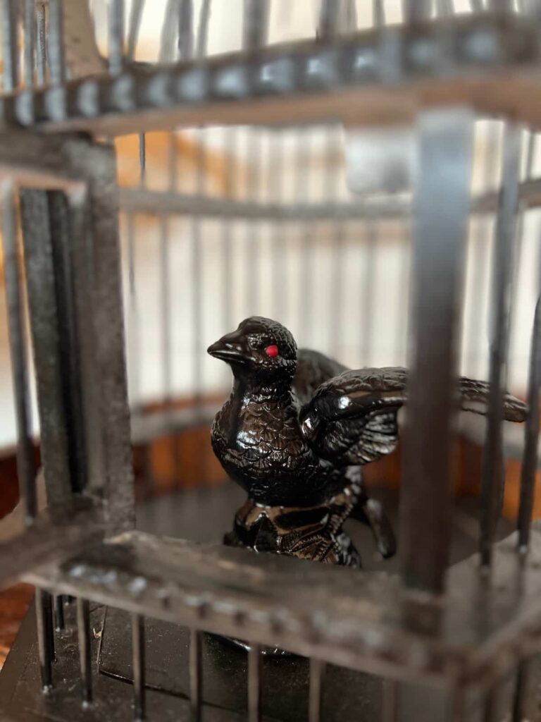 image shows painted bird figurine in a cage.