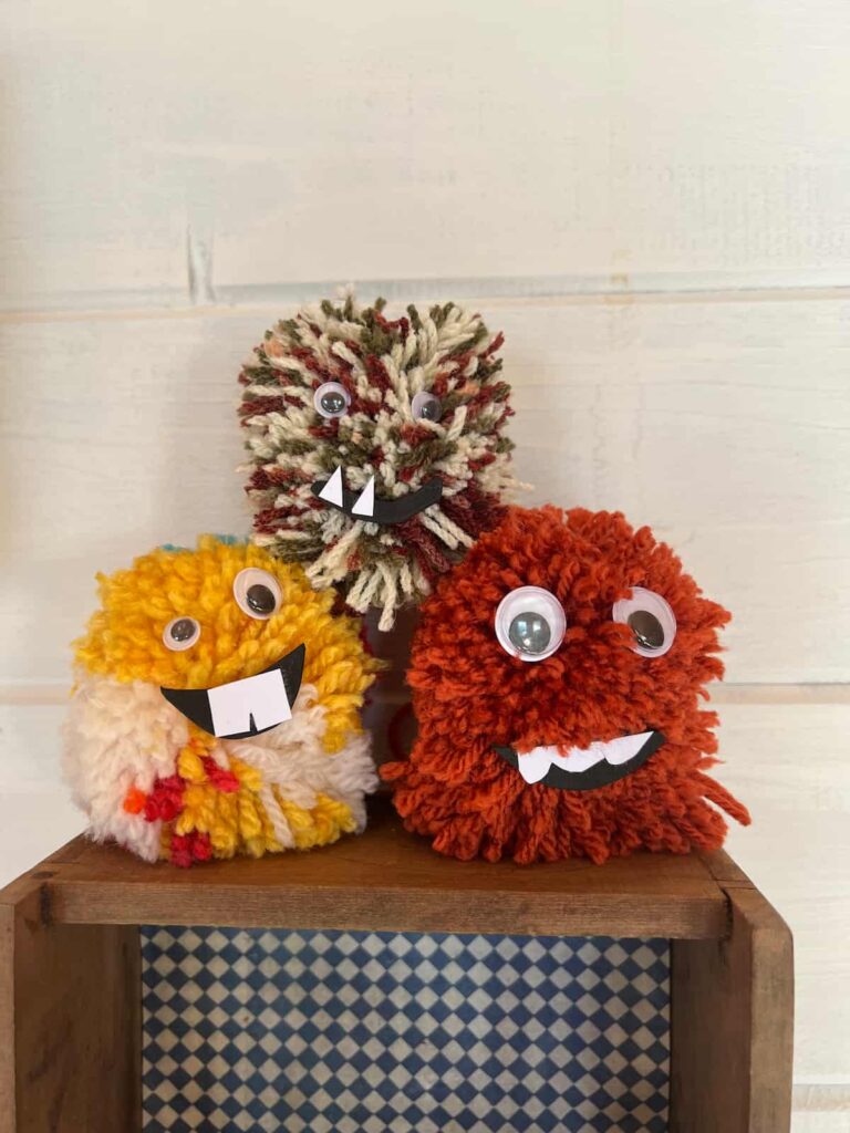 image shows three pom pom monsters on shelf.