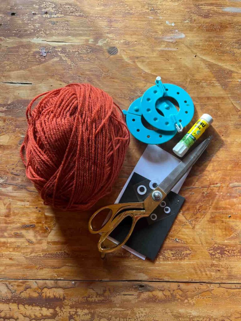 image shows yarn, scissors and pom pom maker on a table.