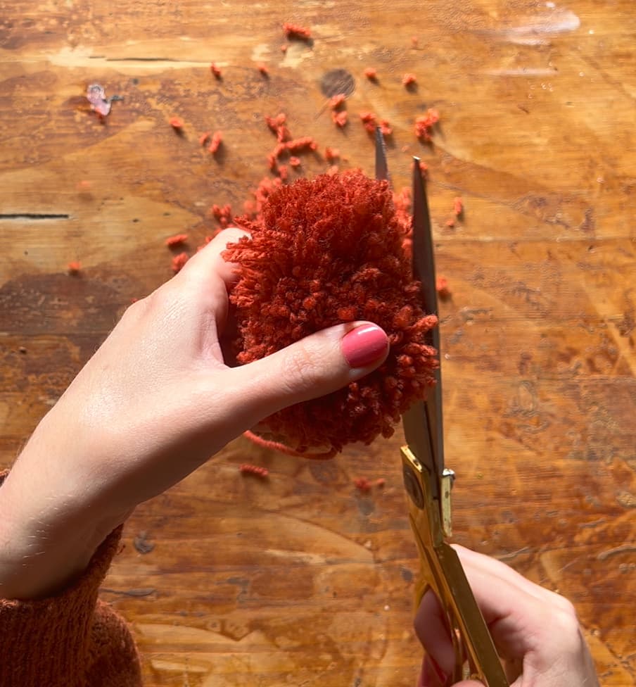 image shows trimming pom pom strands with scissors.