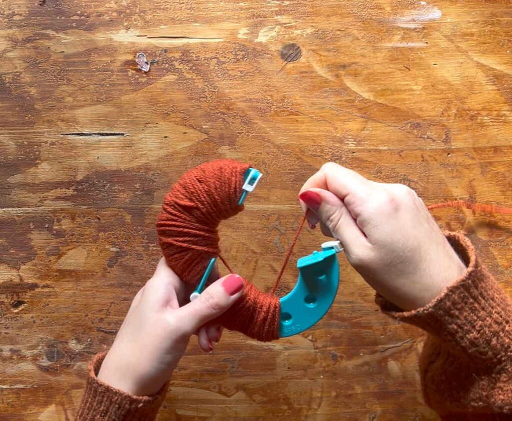 image shows wrapping yarn around pom pom maker.