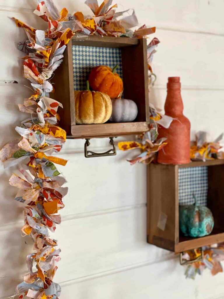 image shows rag garland draped over shelves on a wall with pumpkins.