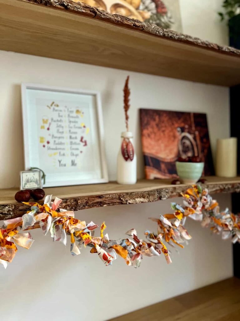 image shows rag garland attached to a shelf with pictures and vase on.