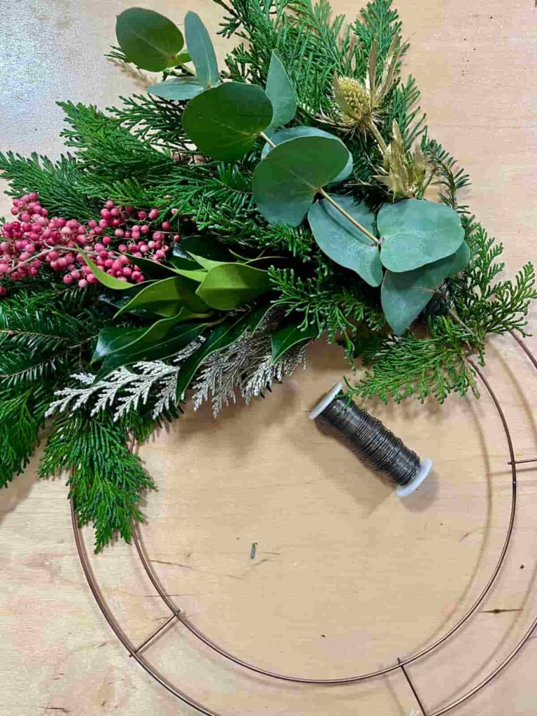 image shows greenery bundles attach to metal hoop wreath.