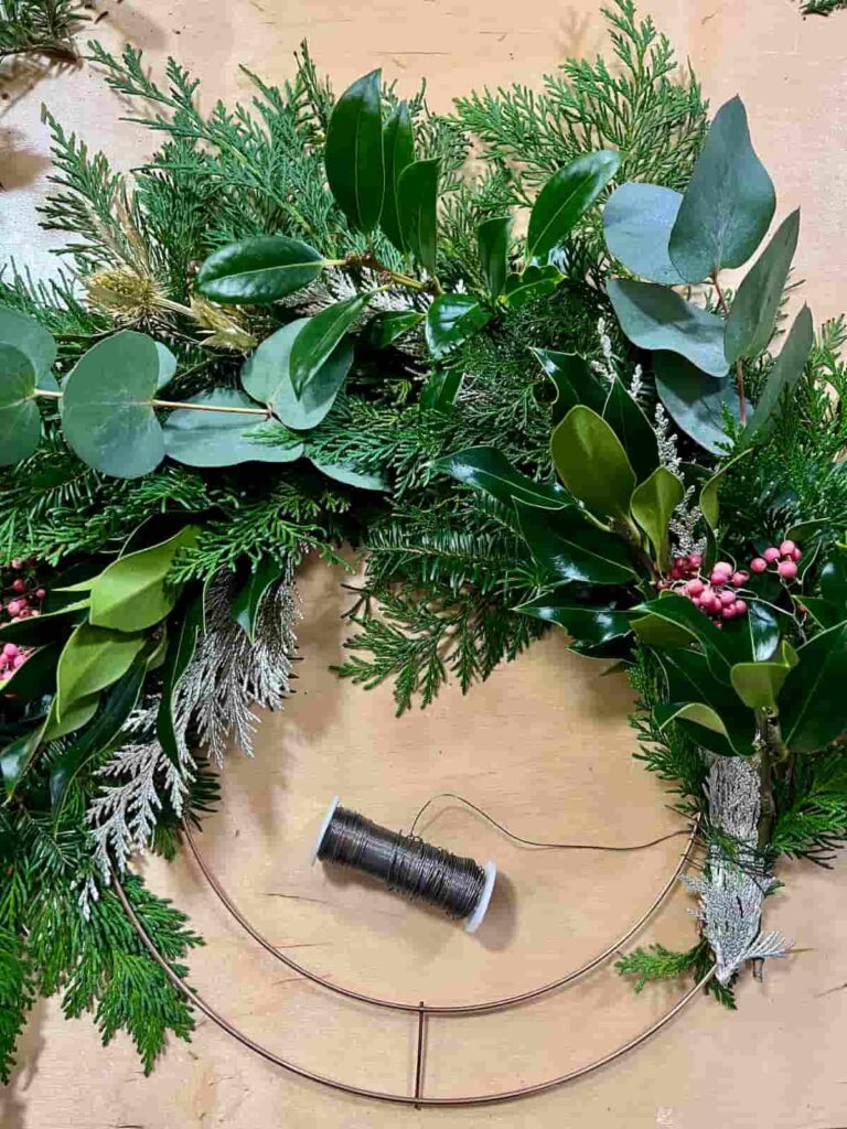 image shows progress on adding greenery bundles to metal wreath.