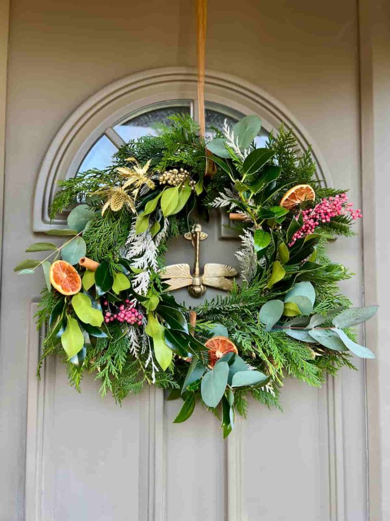 image shows christmas wreath made with metal hoop and greenery on front door.