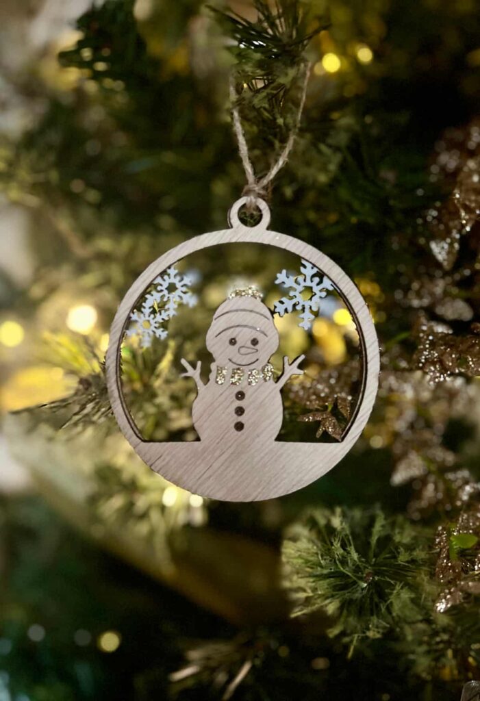 image shows laser cut snowman ornament on a tree.