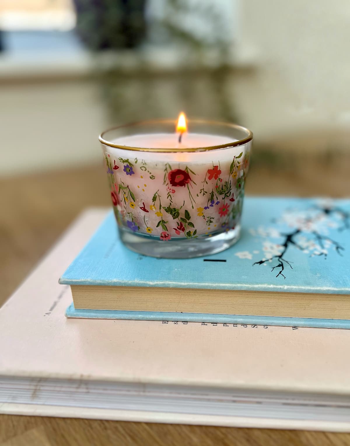 image shows handmade candle on floral glass jar on top of books.