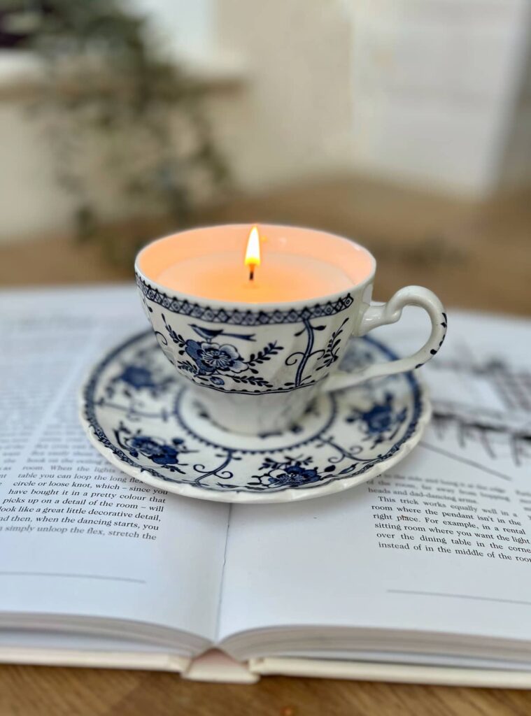 image shows lit candle in a tea cup on an open book.