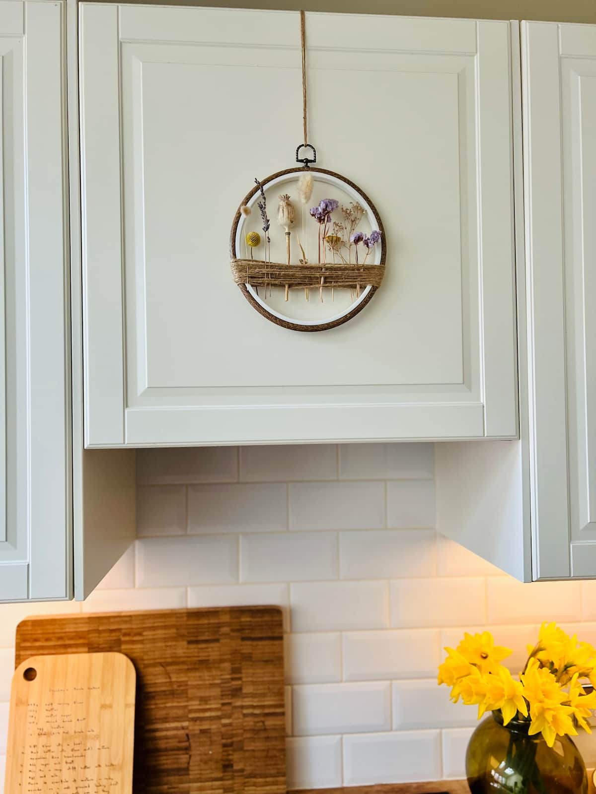 image shows dried flower embroidery hoop on kitchen cabinet.