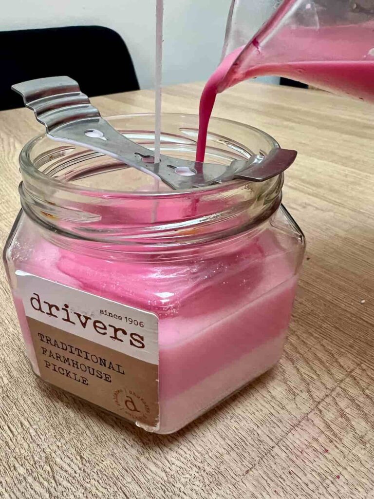 image shows pouring coloured wax into upcycled pickle jar.