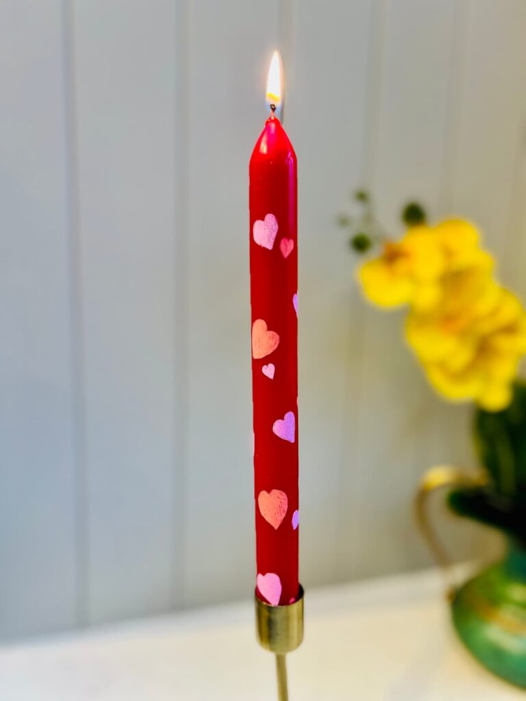 image shows red taper candle painted with hearts.