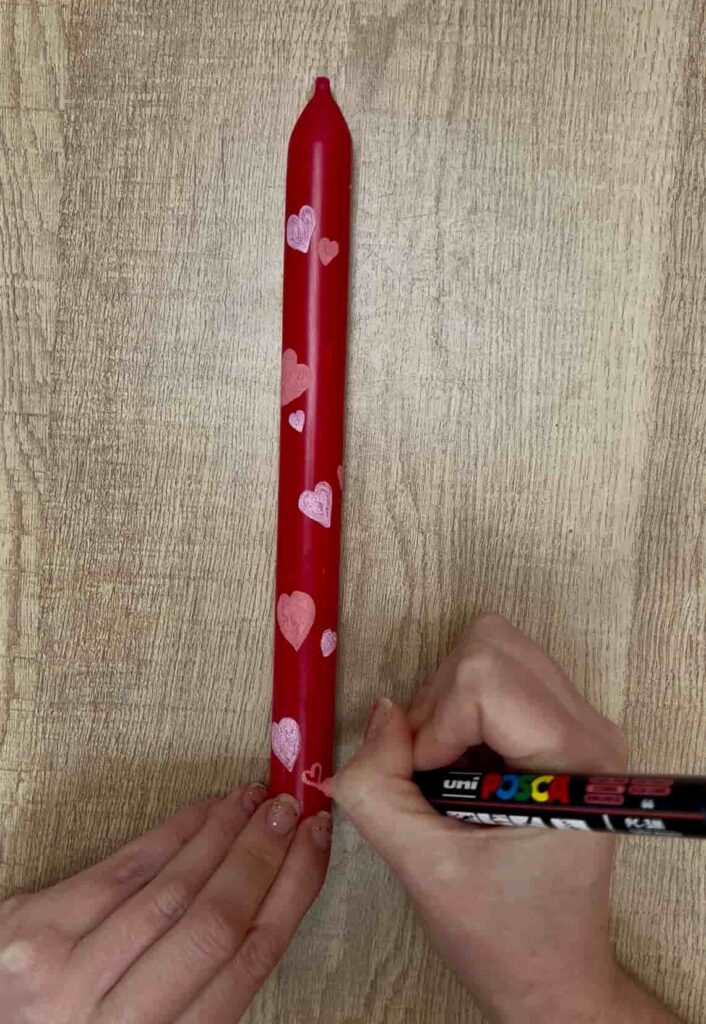 image shows painting hearts on a red taper candle.