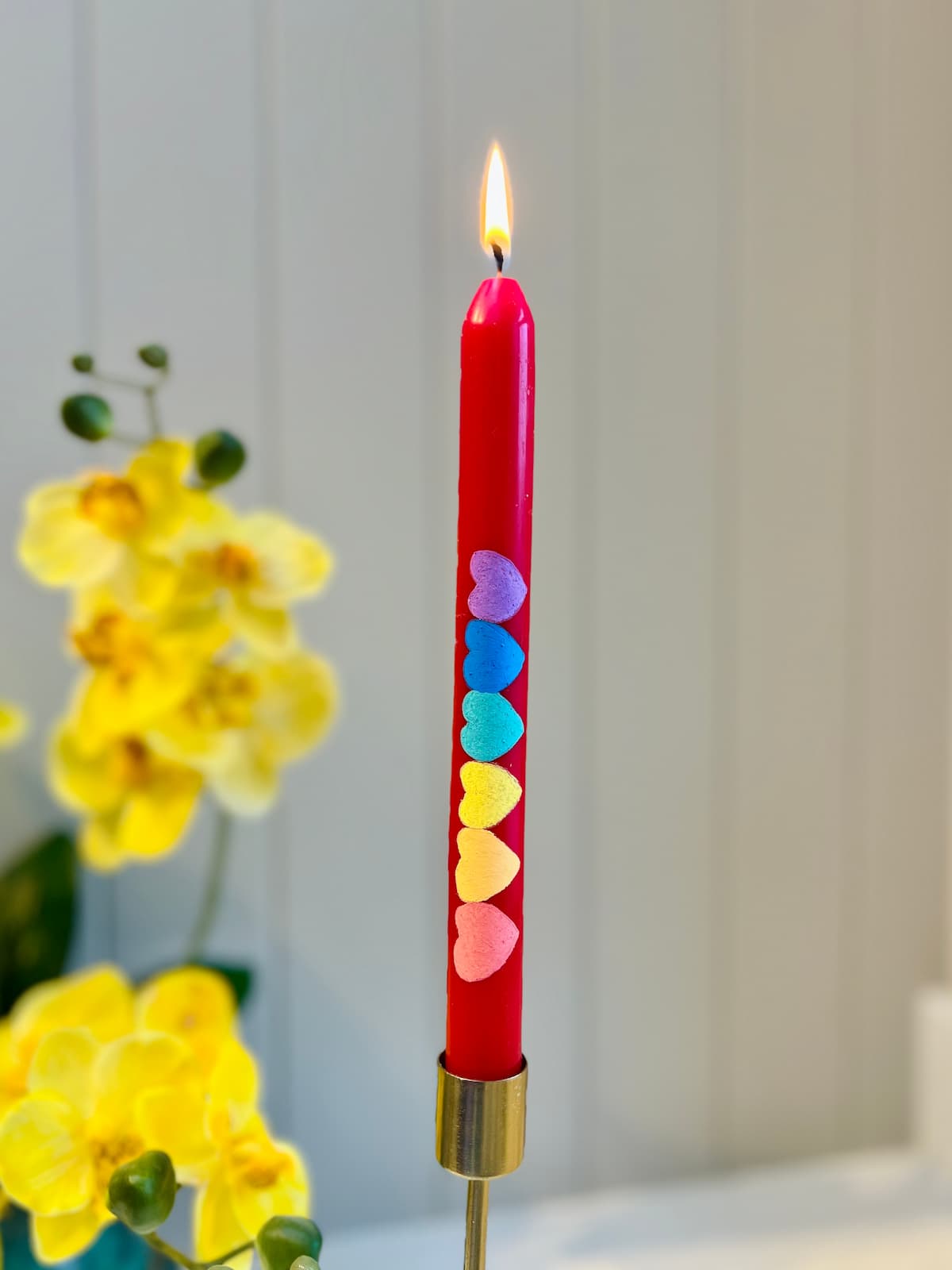 image shows red dinner candle painted with rainbow coloured hearts.