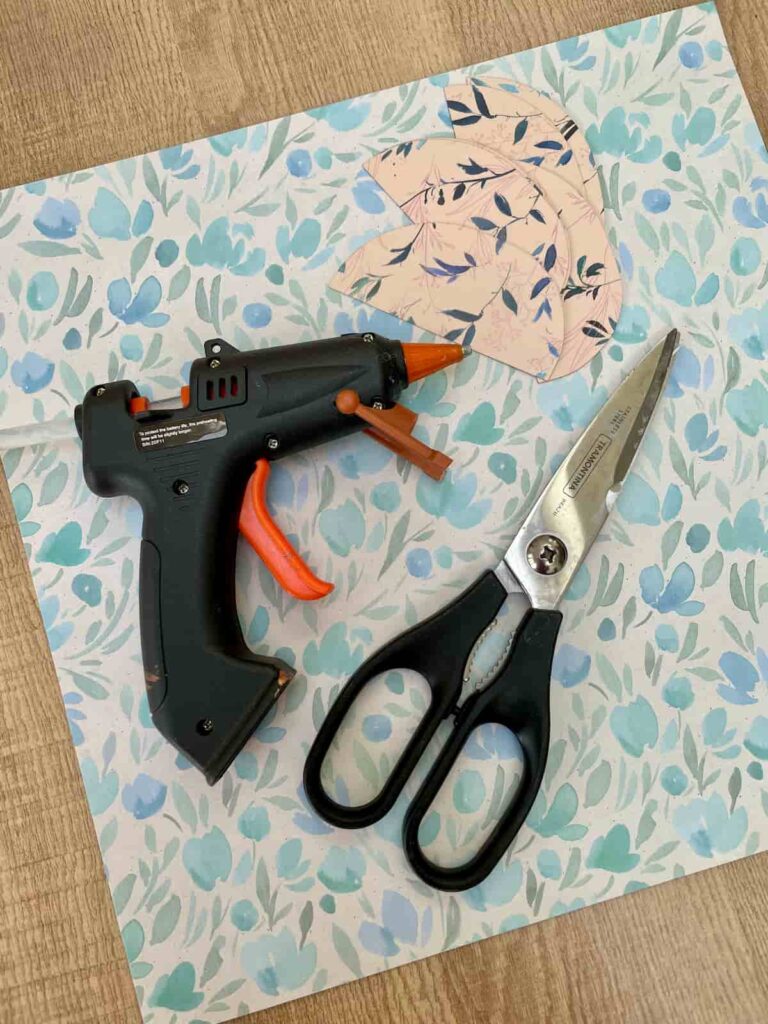 image shows floral paper, a glue gun, cut out paper and scissors.